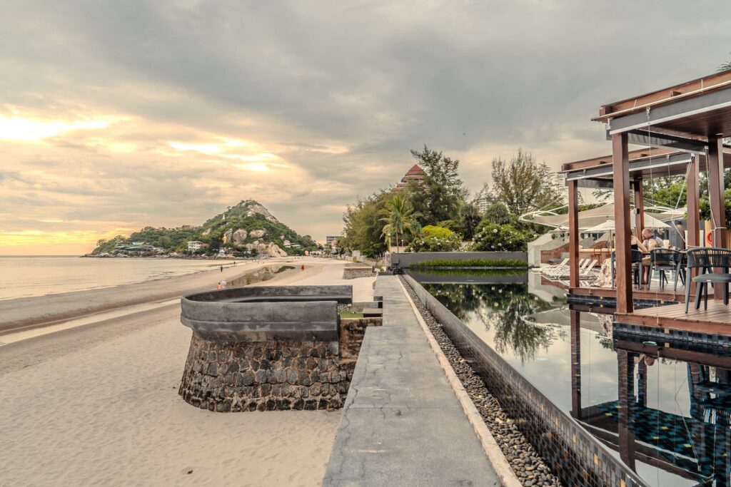 Beachfront walkway beside the infinity pool at The Yana Villas, with Khao Takiab hill at dusk